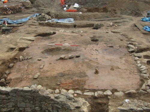 Looking south across a stone boundary wall at the Roman building. Note the opus signinum floor has buckled and collapsed in places.