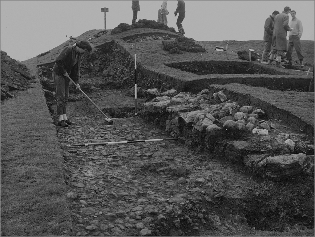 The hillfort entrance passage during excavation in 1960, showing the cobbled road surface, the base of the drystone wall and large post holes that supported the gates. Image: ULAS